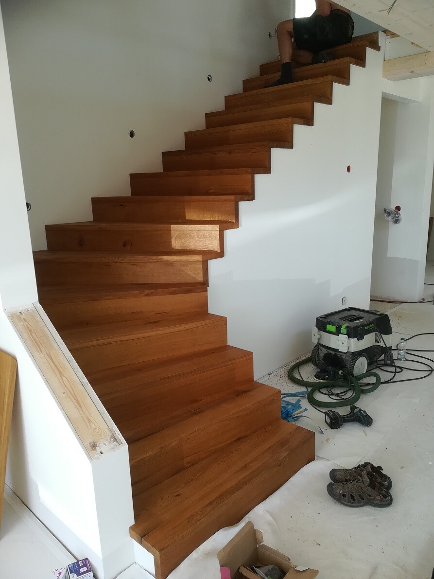 Moderne Holztreppe im Innenraum, Bauarbeiten; Werkzeuge, Schuhe und Material am Boden; Person oben.