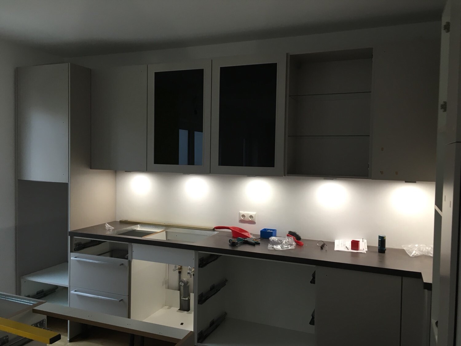 Moderne Küche im Bau mit Hängeschränken, offenen Regalen und Arbeitsplatte mit Werkzeugen.