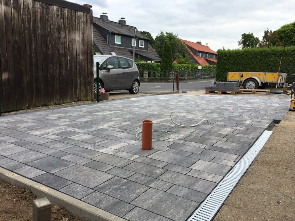 Frisch gepflasterte Hoffläche aus grauen Pflastersteinen; orange Rohr und Schlauch im Vordergrund.