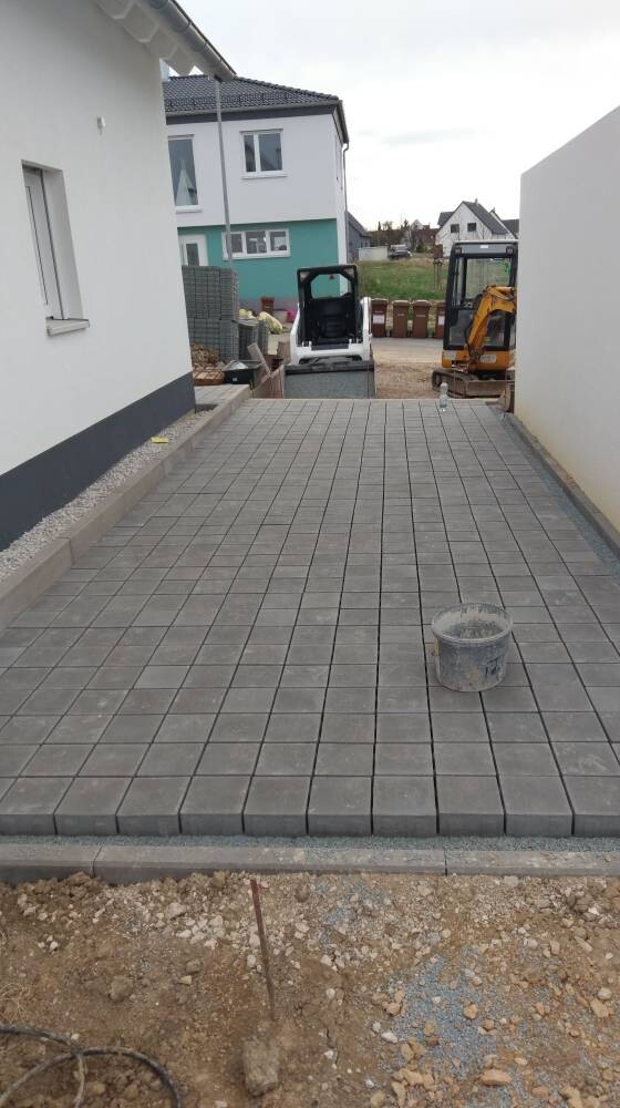 Gepflasterte graue Einfahrt zwischen Gebäuden; Baugeräte im Hintergrund