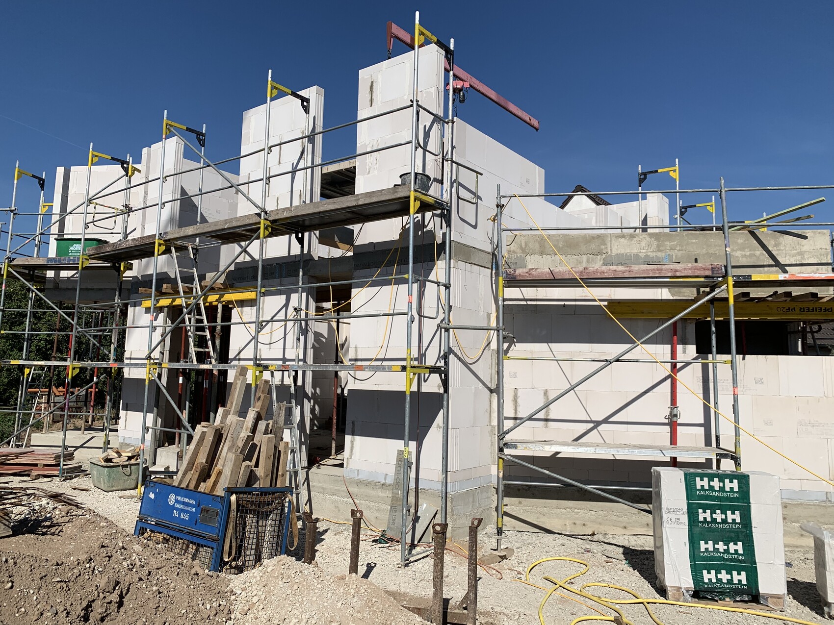 Baustelle mit Gerüst, weißer Porenbeton-Wand und Baumaterialien.