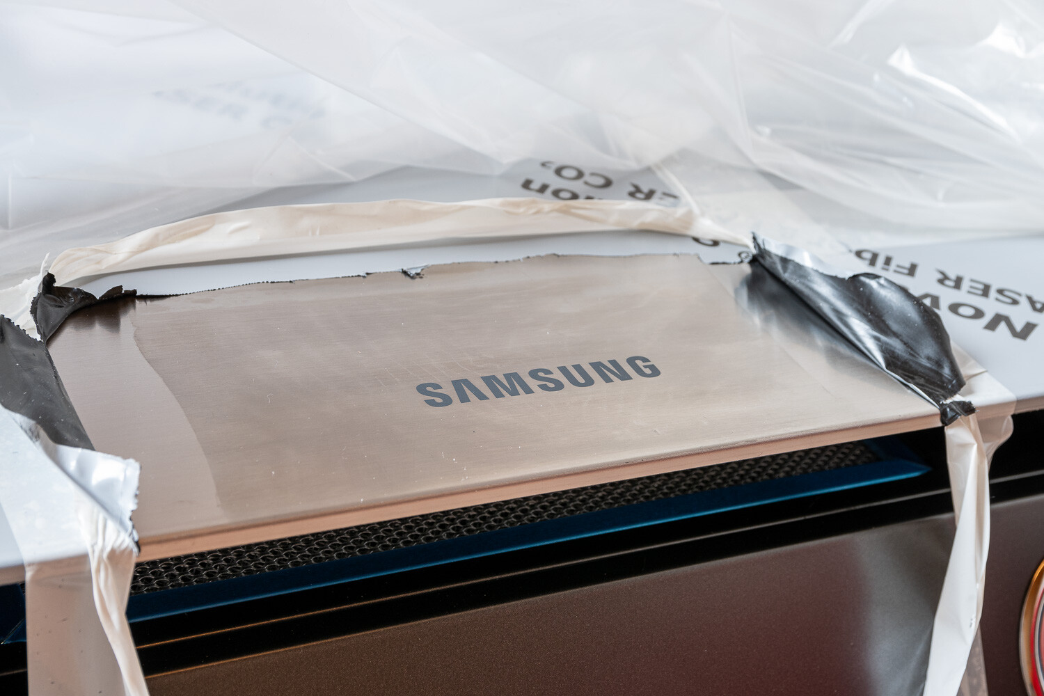 SAMSUNG-Logo auf Edelstahlgerät, von Verpackung und Schutzfolie umgeben.
