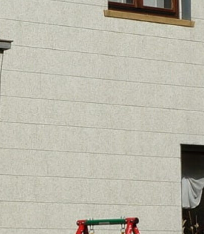 Helle Außenwand mit strukturierter Putzoberfläche, kleines Fenster oben, Baugerüst am unteren Rand.