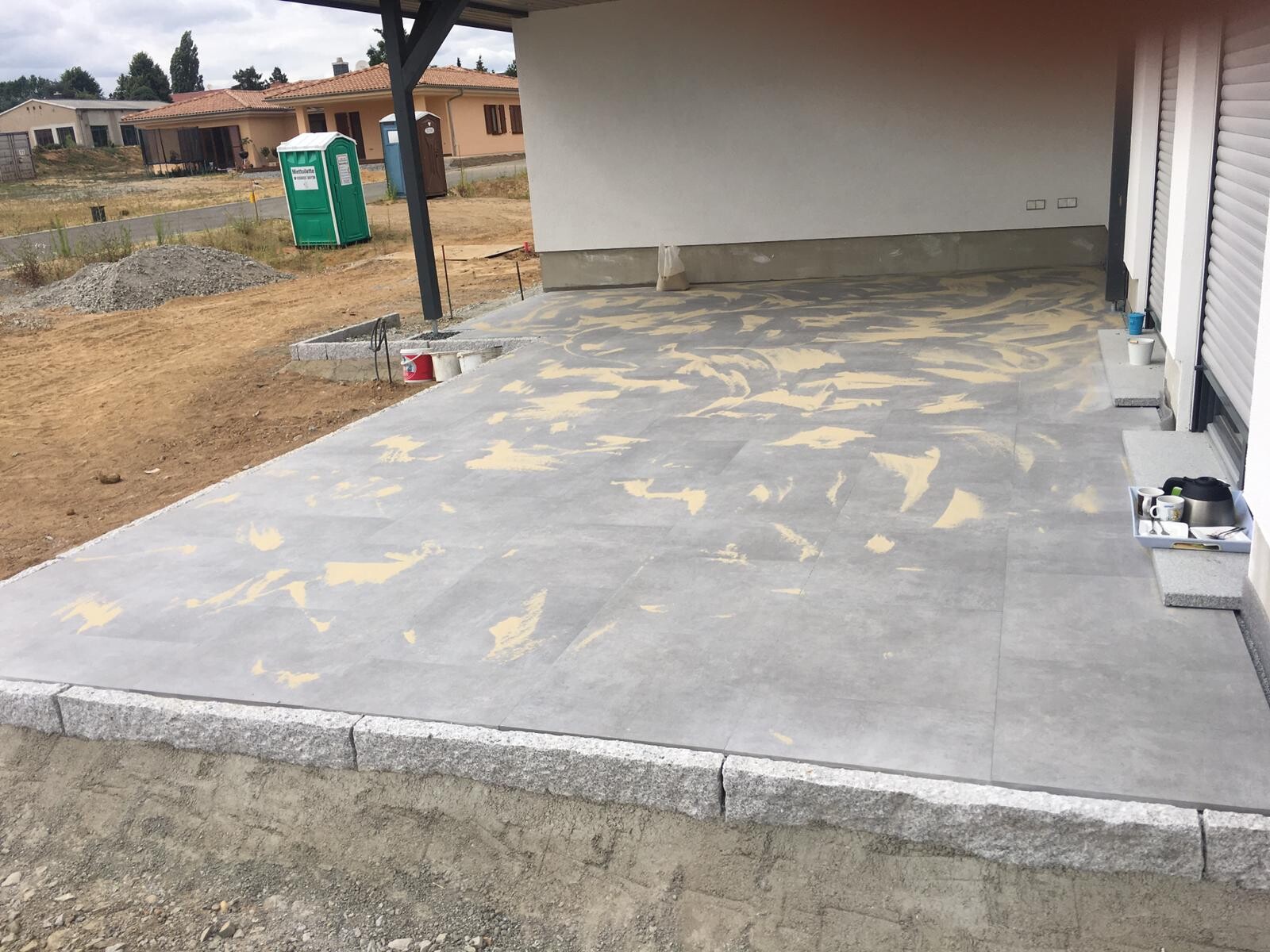 Neue graue Terrasse vor dem Haus, Baustellenbereich mit Werkzeugen und Porta-Potti im Hintergrund