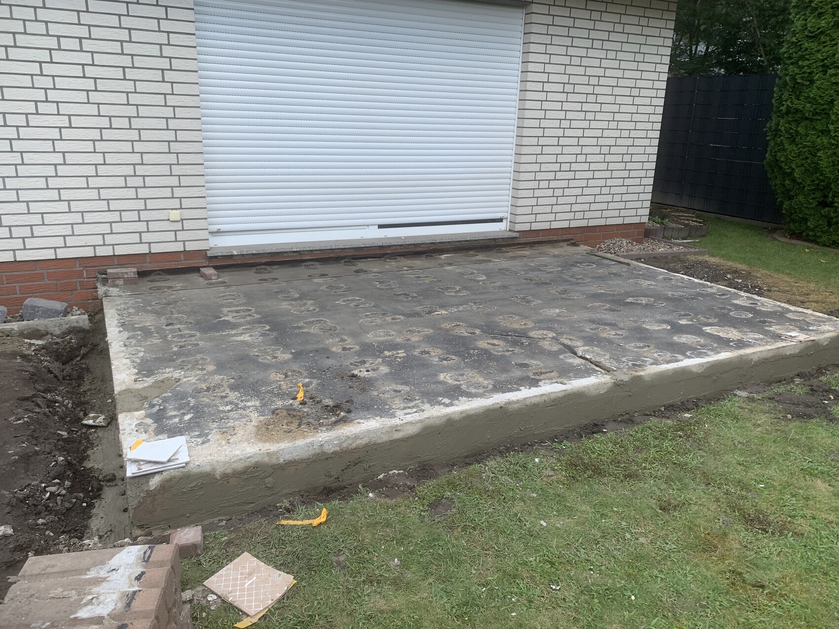 Außenansicht eines Hauses mit einer Beton-Terrasse vor der Garage; weißer Rollladen, runde Muster auf dem Boden.