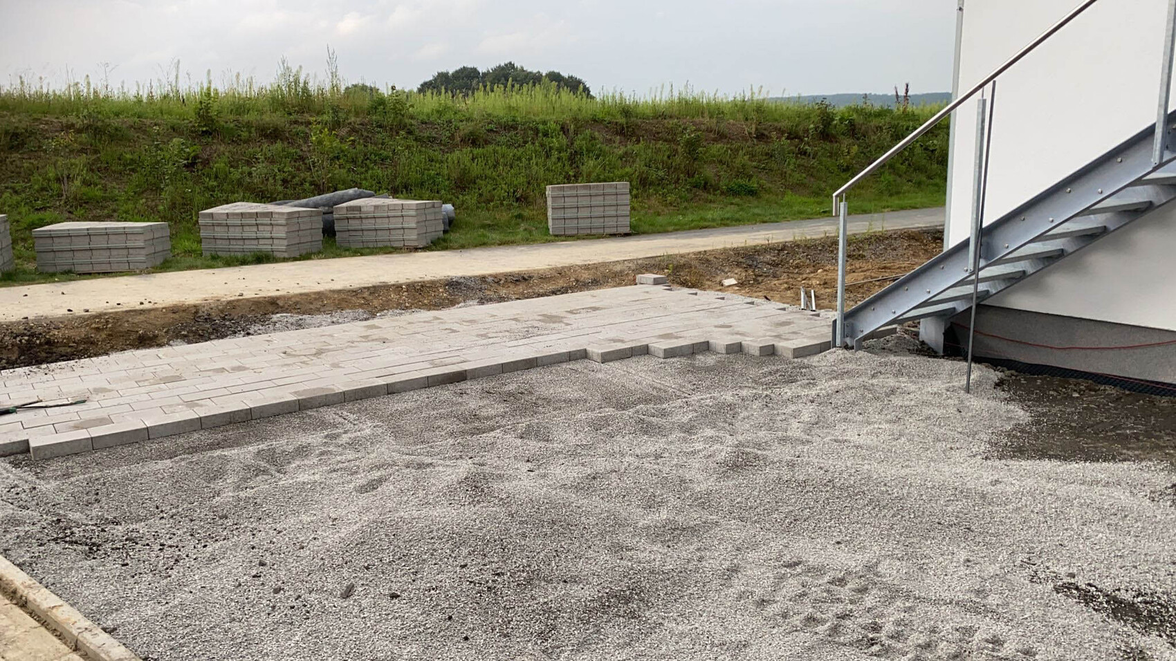 Gepflasterte Baustelle: Pflastersteine, Stapel Betonplatten, Metalltreppe rechts.
