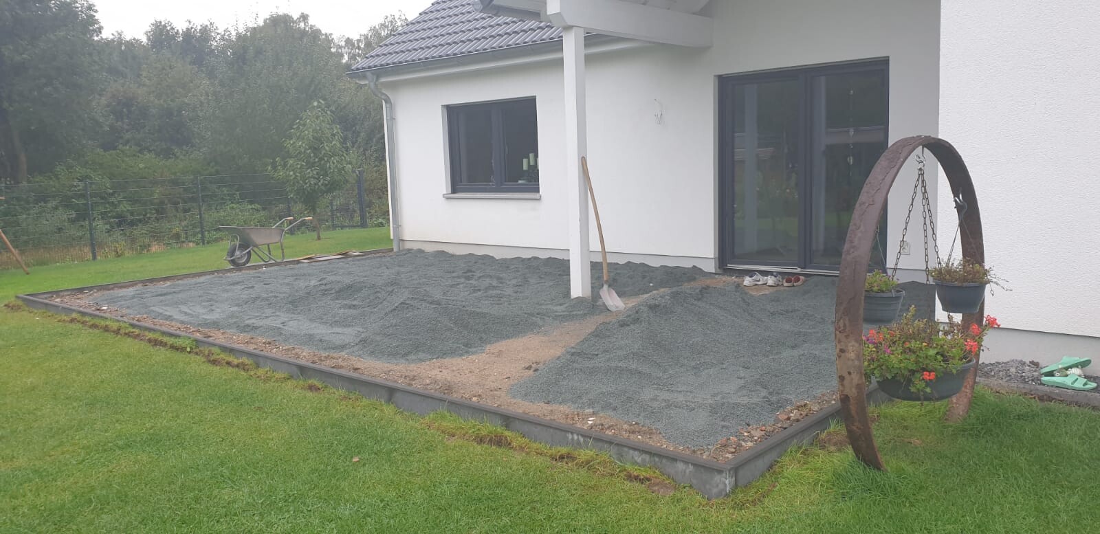Gartenbereich vor dem Haus: Kiesunterlage wird als Terrasse angelegt, Schaufel und Pflanzkübel.