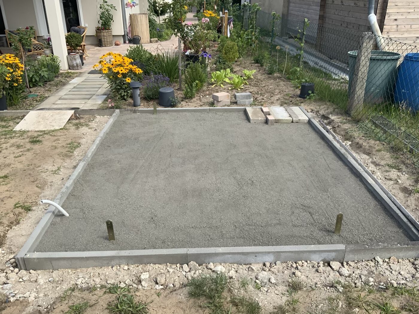 Gartenbaustelle: rechteckige Kiesfläche mit Betonrand, Beete und Gartenweg im Hintergrund.