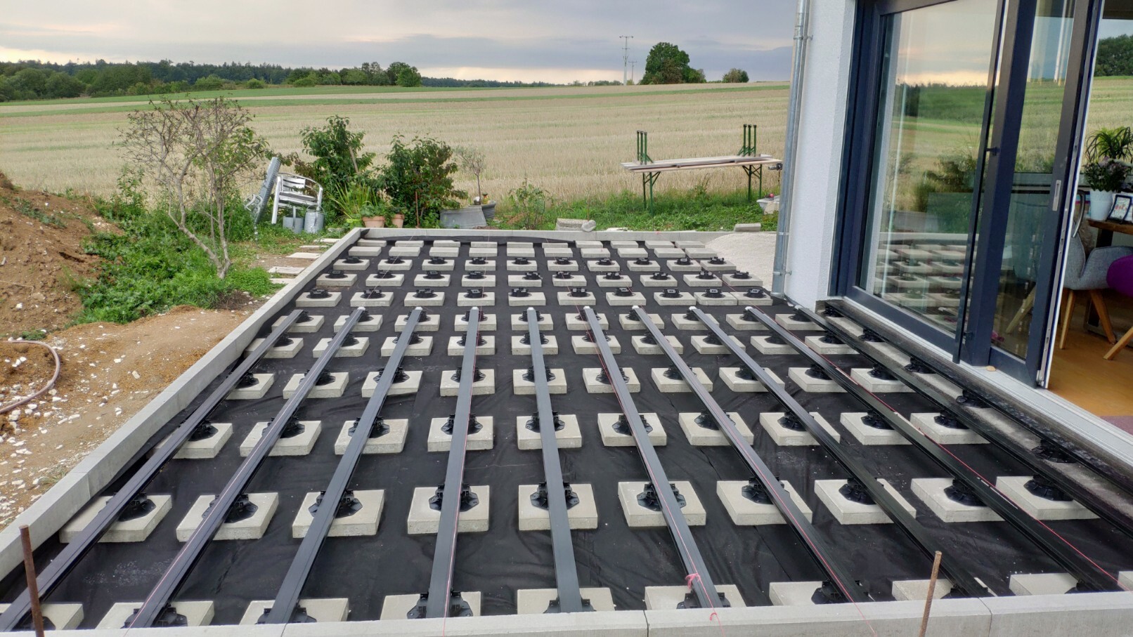 Terrasse im Bau: Heizrohre auf Styropor-Unterlage, schwarze Träger, Glastür rechts.