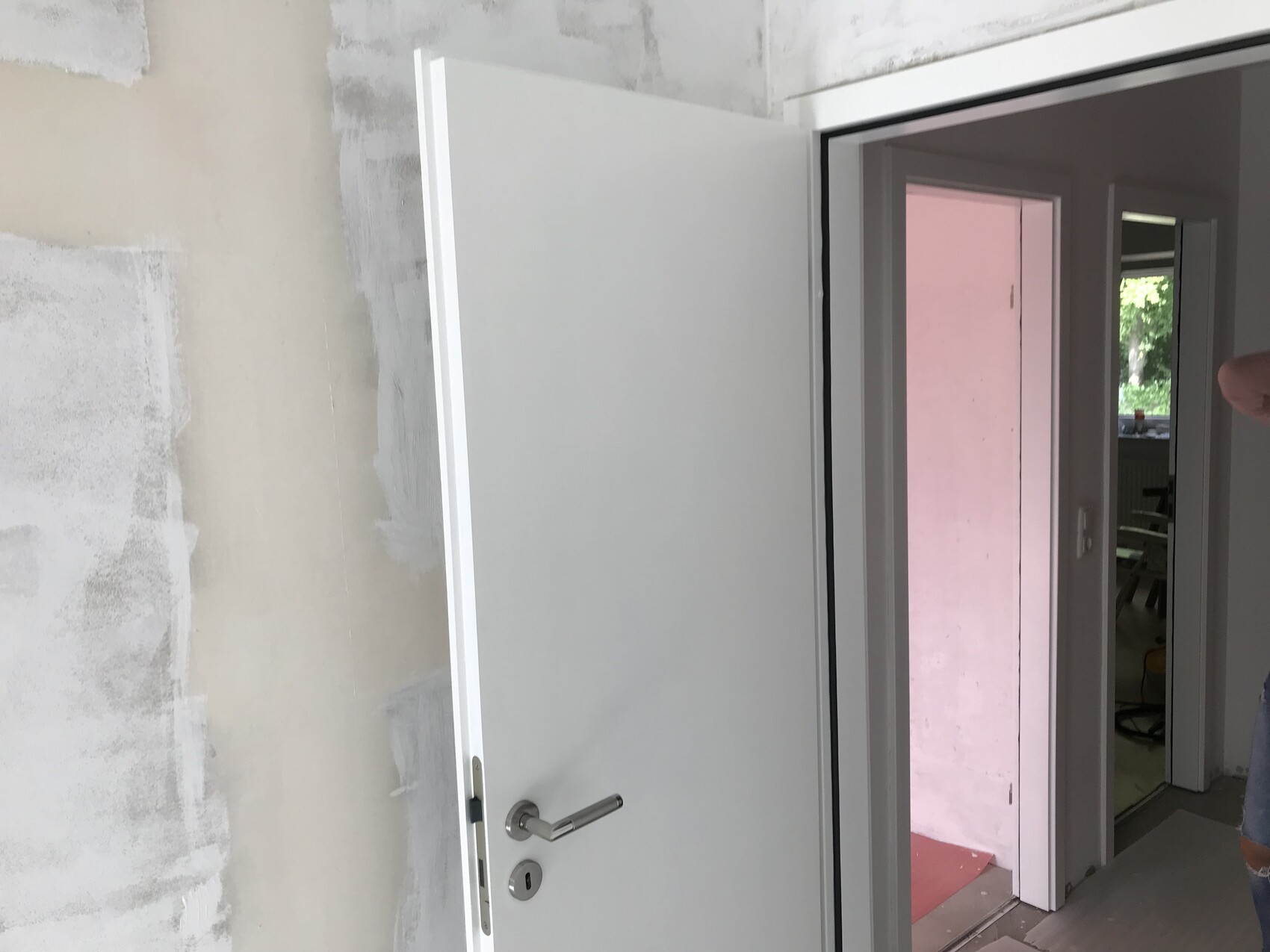 Offene weiße Innentür in Renovierungsraum; ungeputzte Wände, Blick in Raum mit rosa Wand