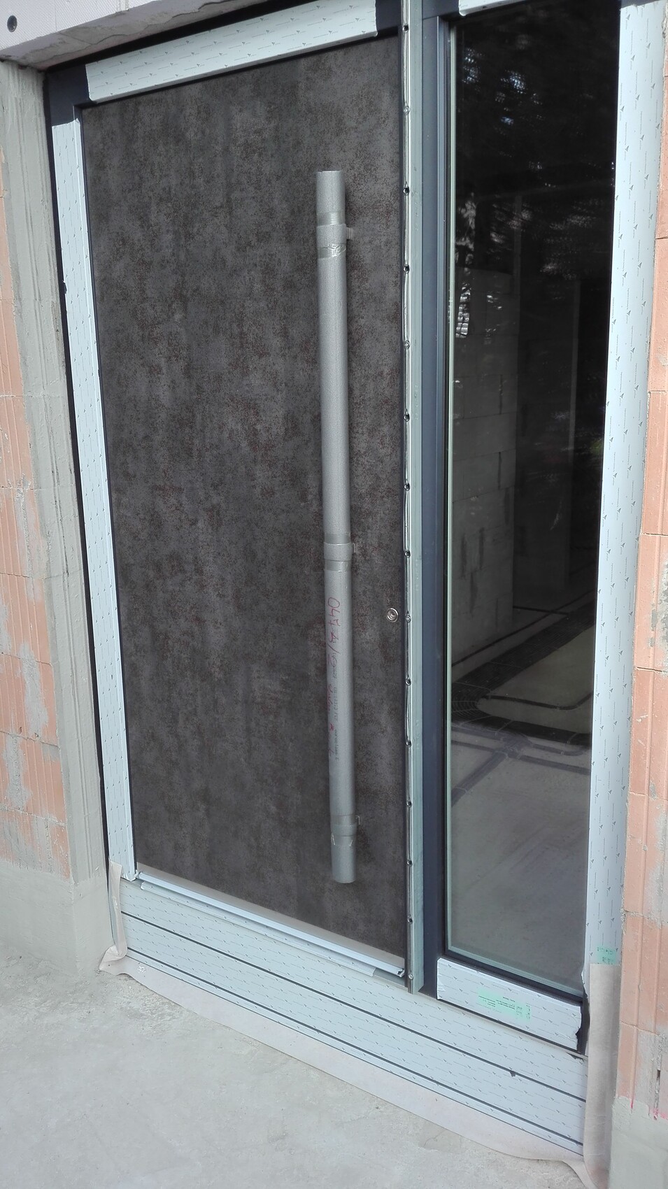 Außentür mit Glasfront; daneben ein vertikales graues Rohr an dunkler Wand.