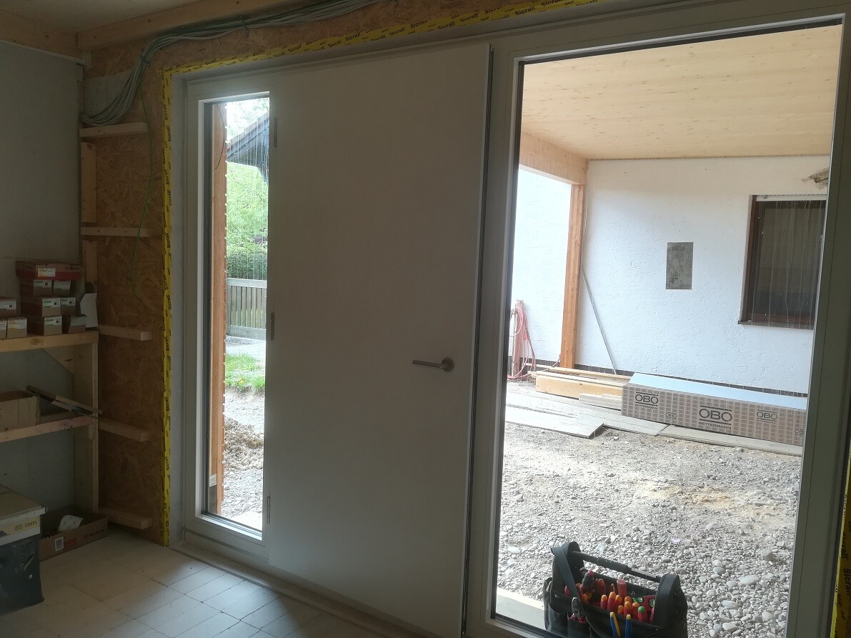Innenraum einer Baustelle: Tür nach außen, Fenster rechts, Bauholz, Werkzeugkorb vorne.