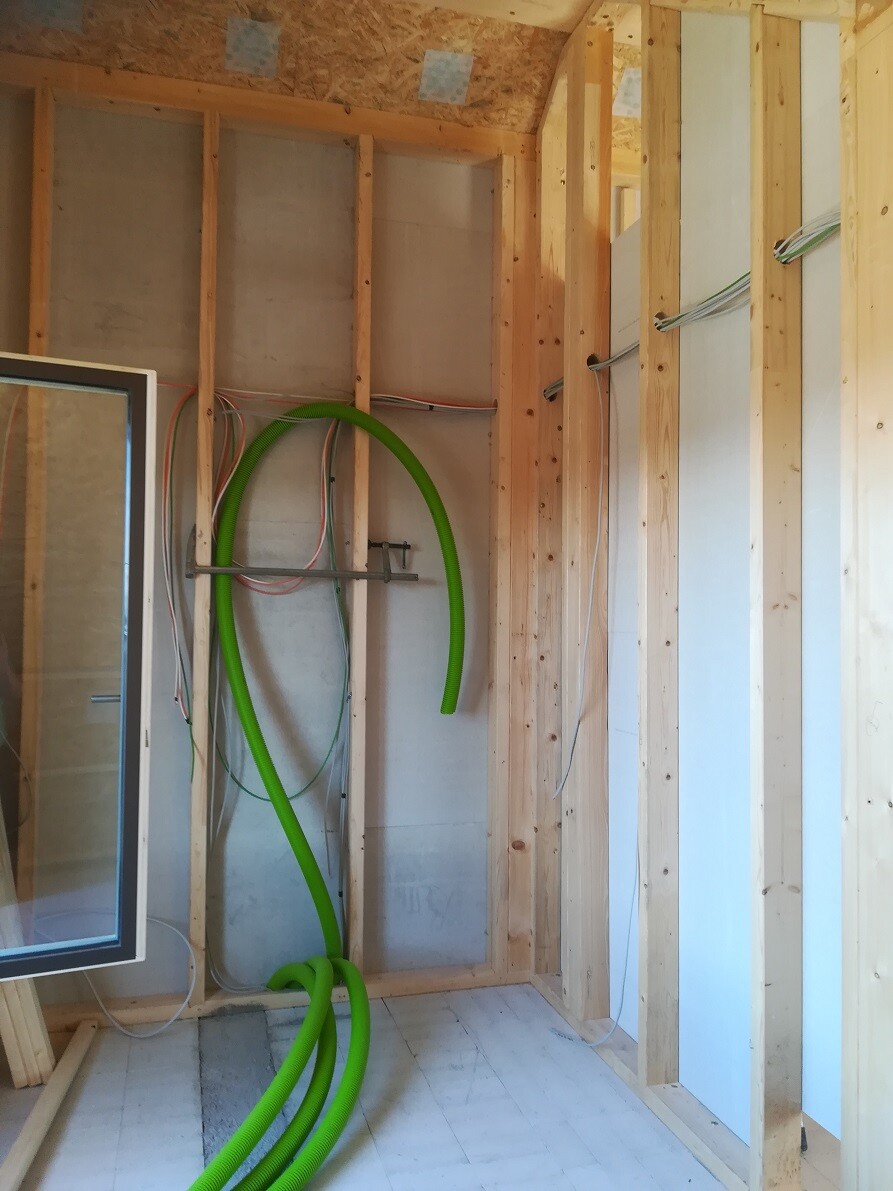 Baustellenraum mit Holzständern, mehreren Kabeln und grünem flexiblem Rohr auf dem Boden