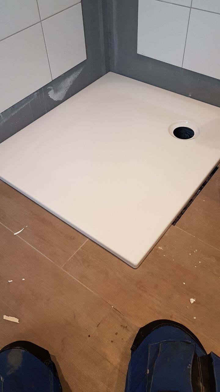 Weiße quadratische Duschwanne in Bad-Ecke; Fliesenwand und Bauarbeiten sichtbar.