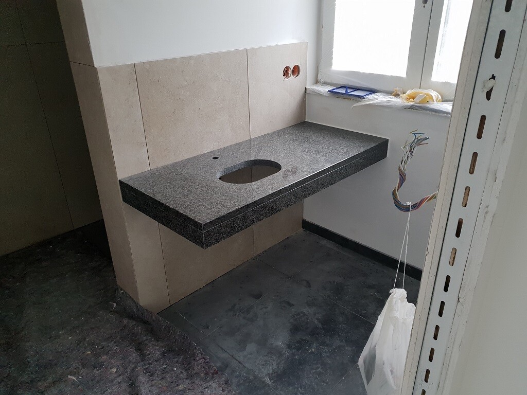 Schwarze Granit-Arbeitsplatte mit Loch für Spüle, beige Fliesenwand und freiliegende Kabel