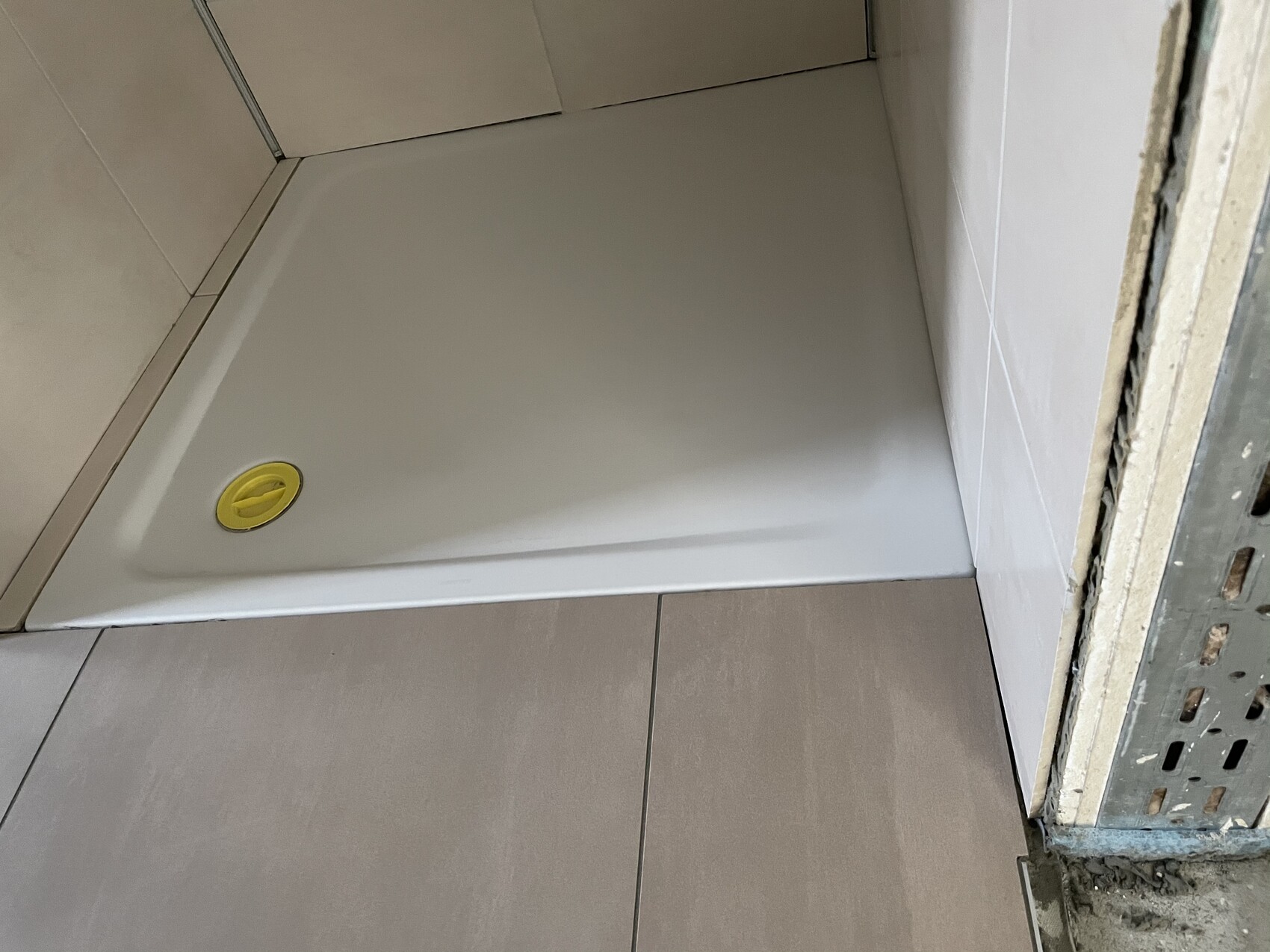 Weißer Duschtrog in Bauphase, gelber runder Abfluss, seitliche Rohbauwand mit Metallrahmen.