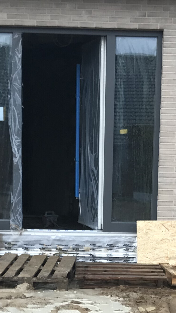 Baustellen-Tür mit Glasfront, Plastikfolie, blaue Stange, Holzpaletten davor.