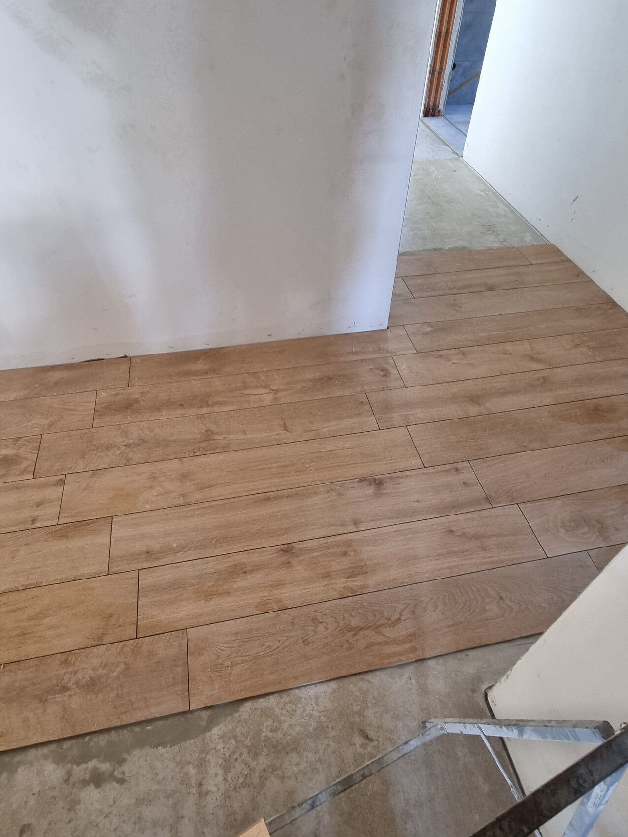 Heller Holzlaminat-Fußboden in einem Flur, Türöffnung im Hintergrund, Treppenzugang rechts.