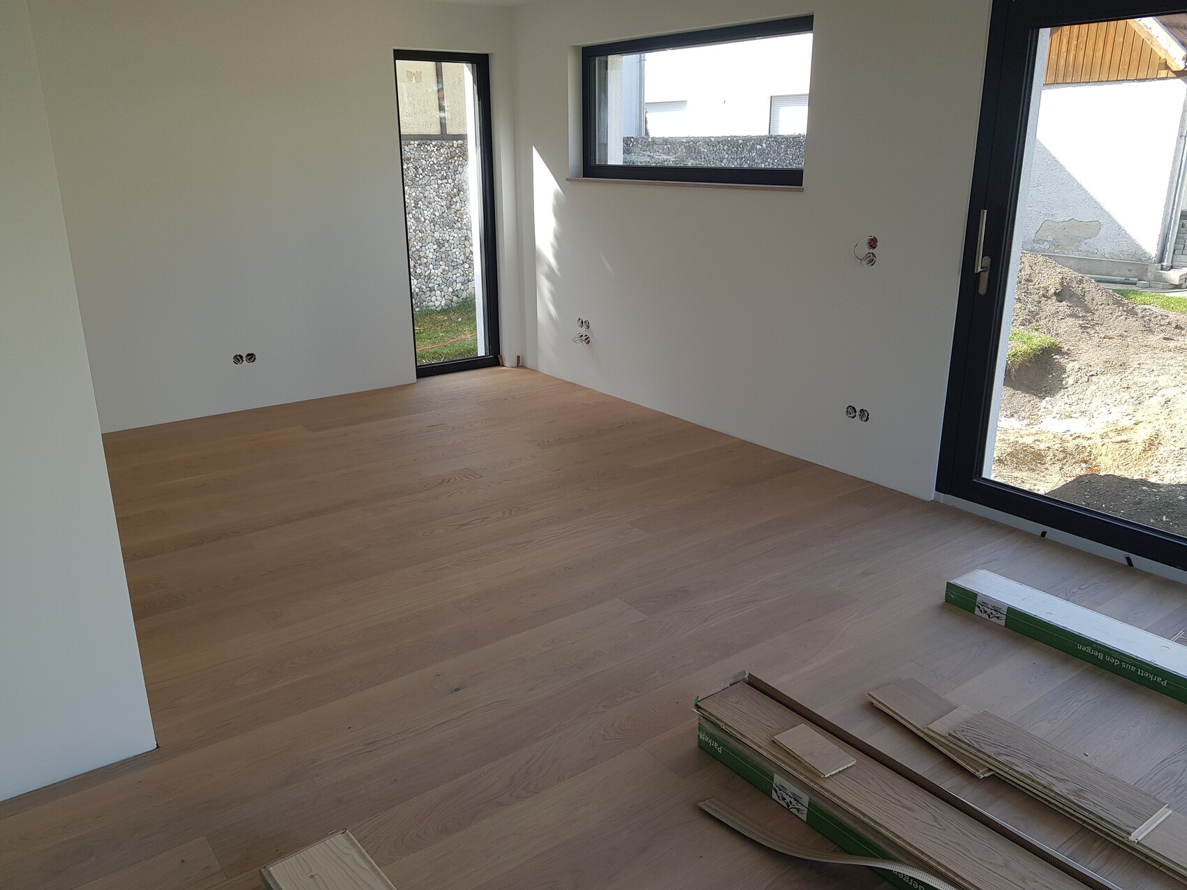 Neues Zimmer mit hellem Holzboden, schwarzen Glasfronten und sichtbaren Elektroinstallationen.