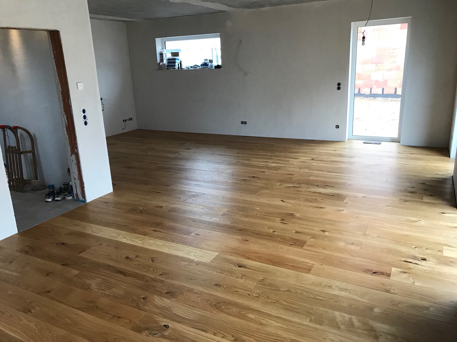 Neu verlegter Holzboden in einem unfertigen Wohnzimmer; Fenster, Tür nach draußen, Bauwerkzeuge.