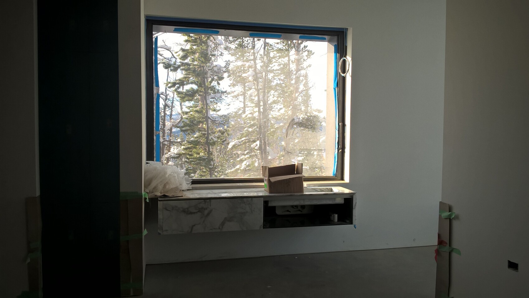 Innenraum im Bau mit großem Fenster, Blick auf verschneite Baumlandschaft; Kartonbox auf Fensterbank