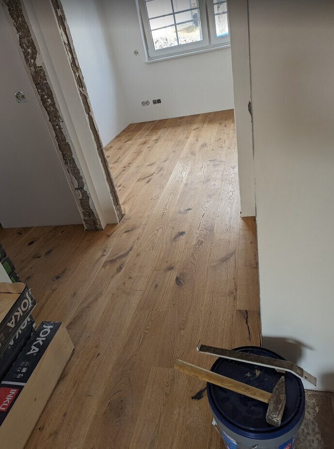 Zimmer im Bau: neuer Holzboden, weiße Wände, Fenster, Werkzeuge und Eimer.