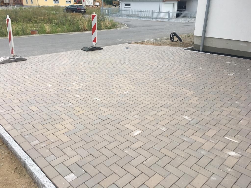 Gepflasterte Fläche aus rechteckigen Steinen, Absperrpfosten links, Gebäude rechts.
