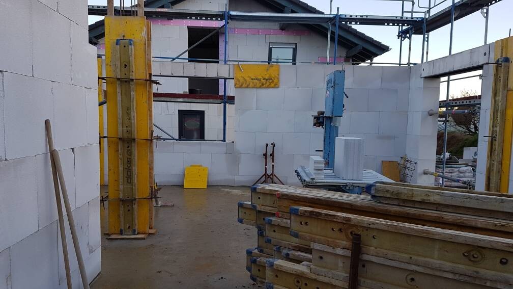 Baustelle mit weißen Betonblöcken, Gerüst, Baugerät und Holzbalken auf dem Boden.