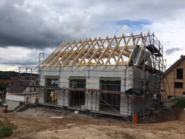 Baustelle: Haus mit offenem Holz-Dachstuhl, eingerüstet, im Wohngebiet.