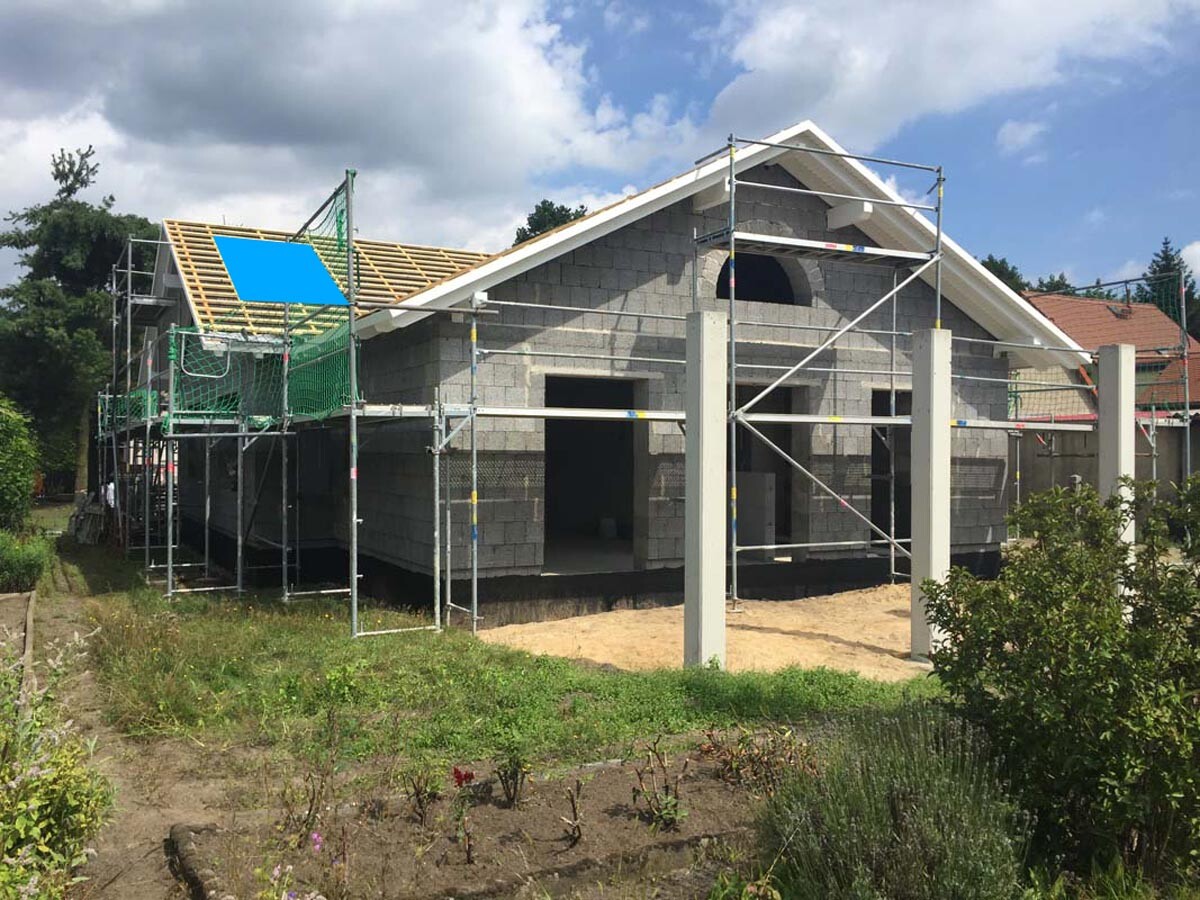 Neubau eines Hauses mit Gerüst, Betonsteinwänden und offenem Eingang; Garten davor.
