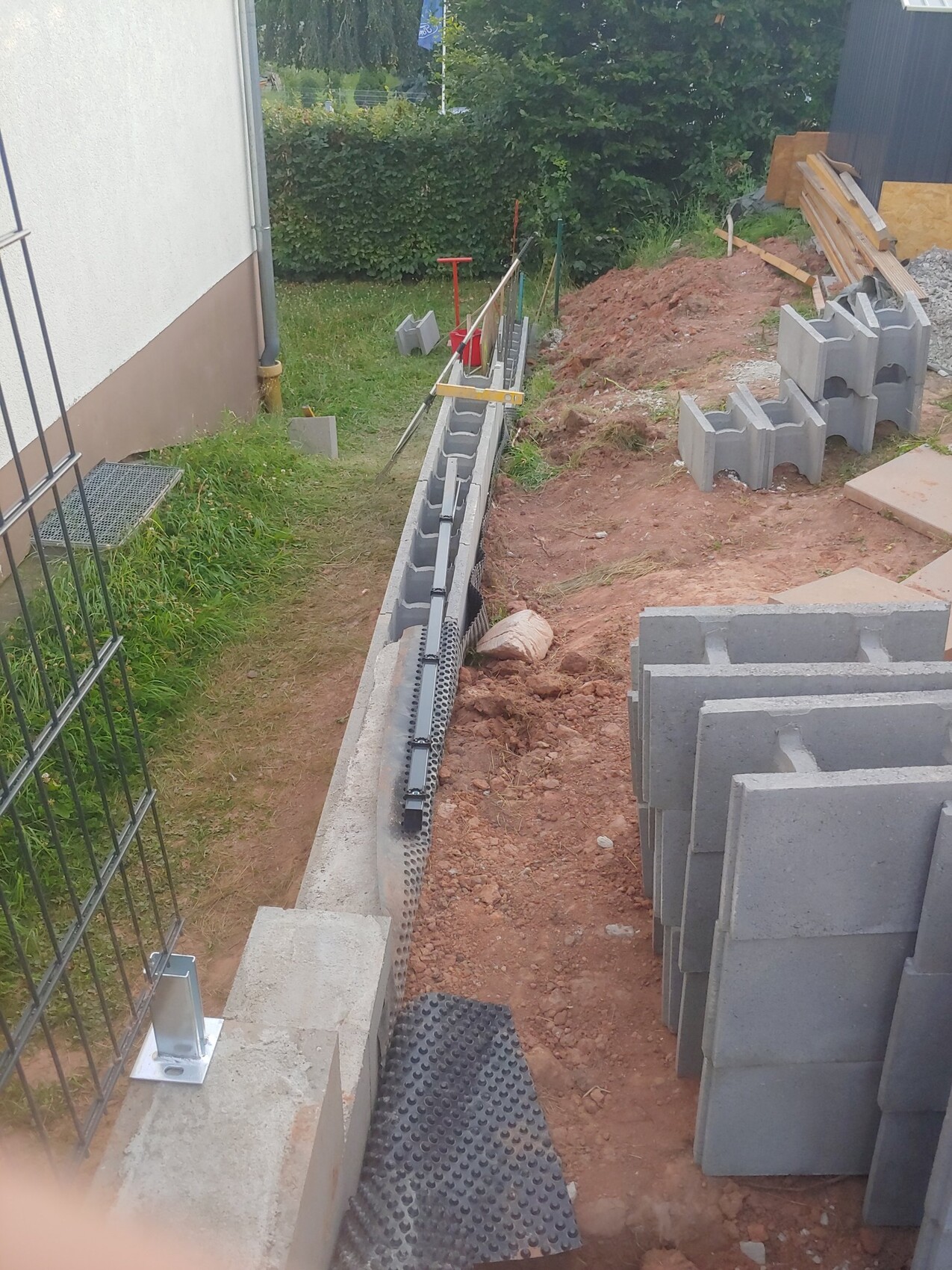 Gartenbaustelle: Betonblockwand im Aufbau, Erdaushub und Bauwerkzeuge.