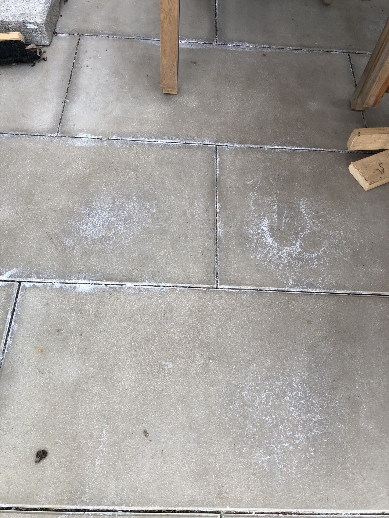 Außenbetonplatten mit weißen Staubspuren zwischen den Fugen; Holzteile eines Tischgestells.