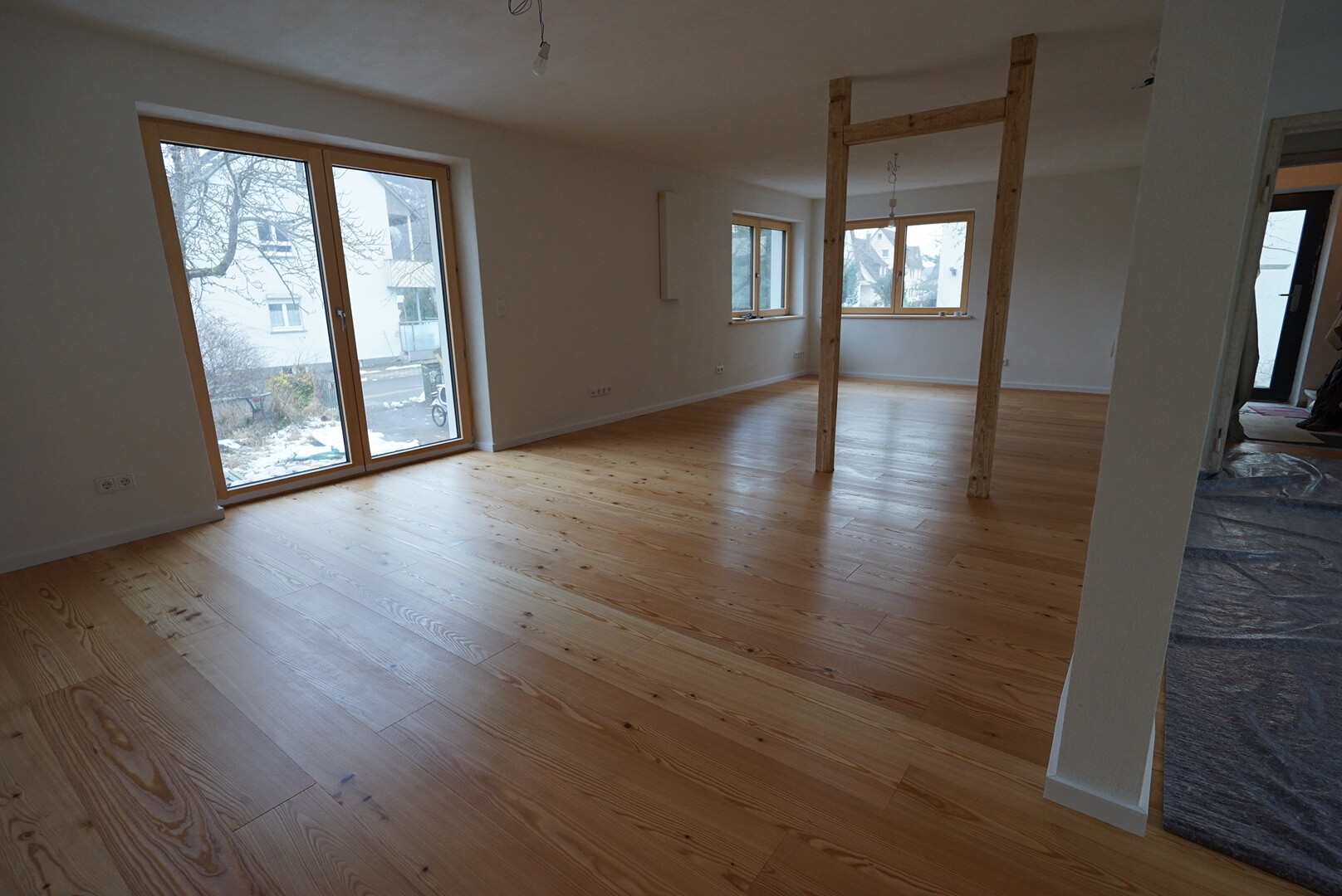 Leerer Wohnraum mit Holzfußboden, großen Fenstern und Holzbalkenrahmen in der Mitte