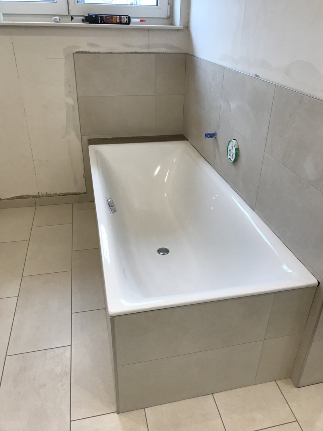 Weiße Badewanne in gefliestem Badezimmer, Baustelle sichtbar.