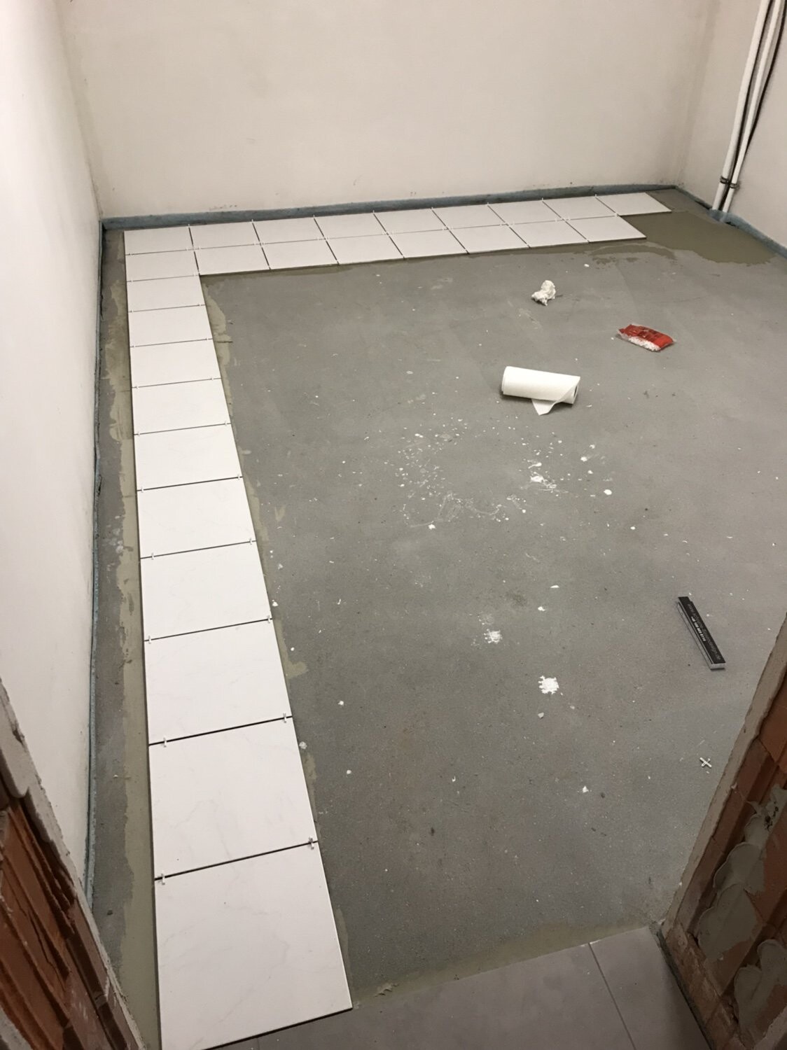 Kleiner Bauraum: Randbereich mit weißen Fliesen, unfertiger Boden, Fliesenreste und Werkzeug.