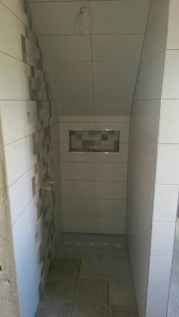 Kleiner Duschraum mit hellen Fliesen, links mosaikartige Fliesenstreifen und Rückwand-Nische.