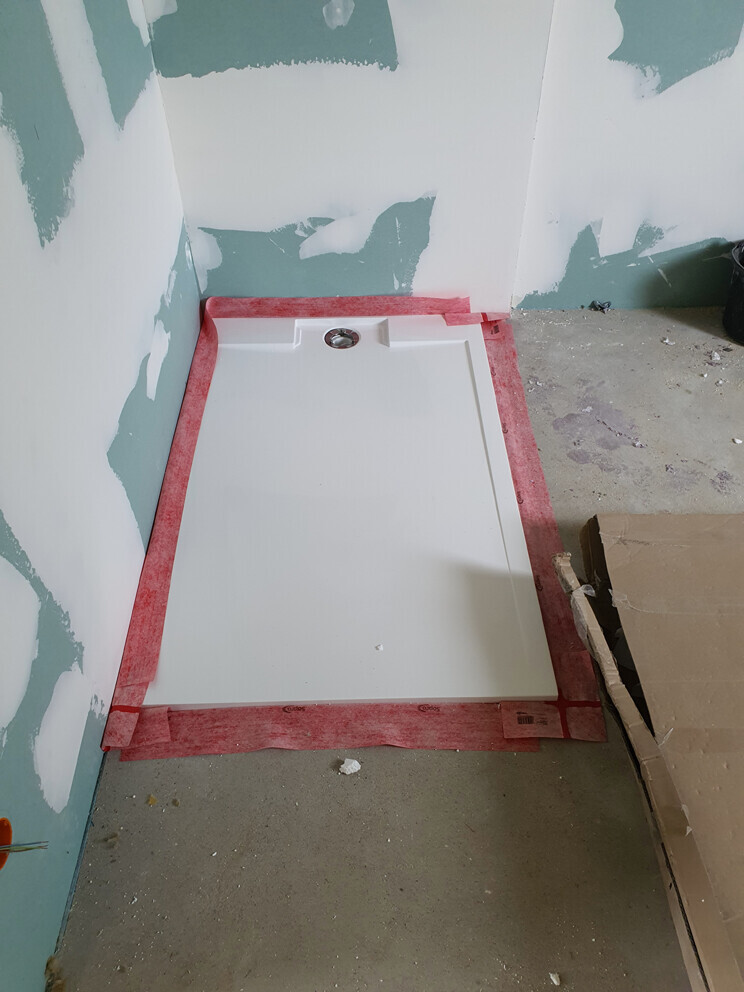 Neue Duschwanne im Rohbau, Rand mit rotem Dichtband und gespachtelten Wänden.