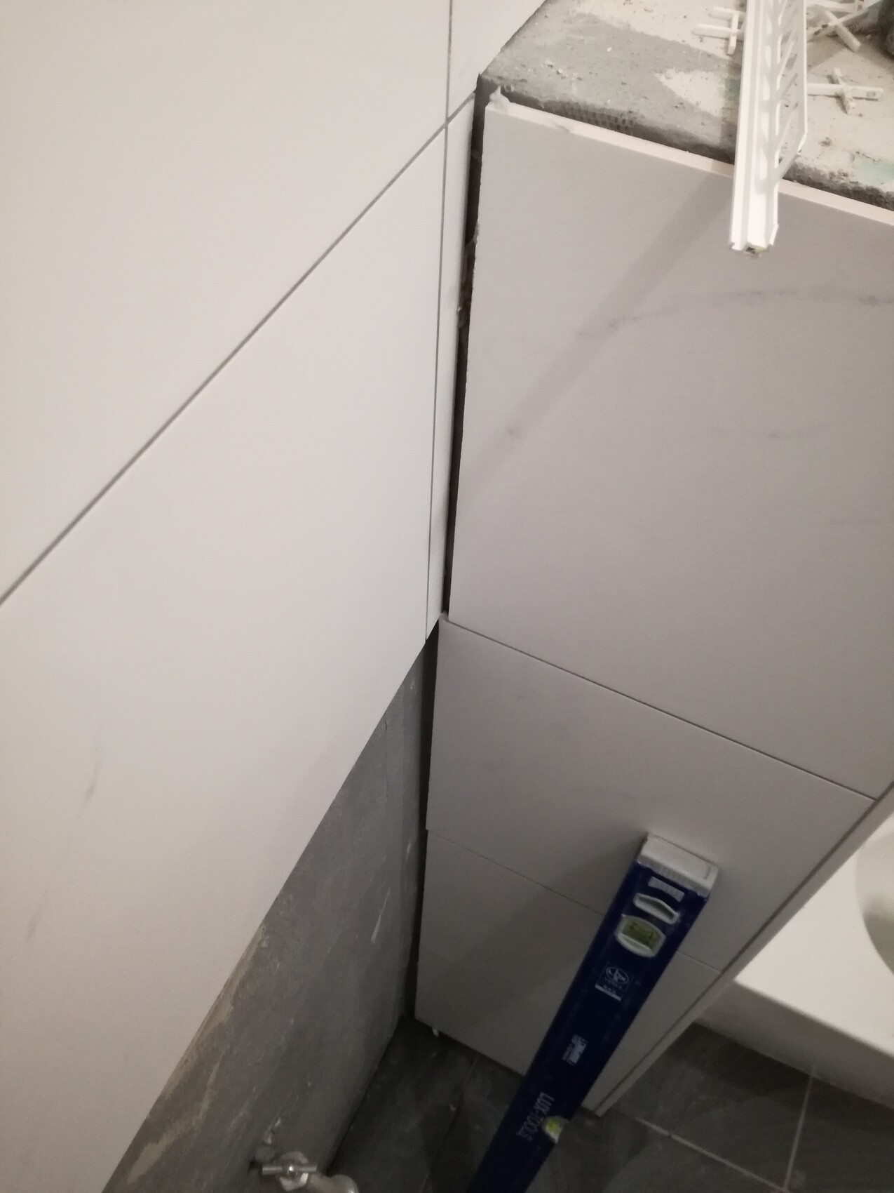 Badezimmer-Baustelle: weiße Wand- und Bodenfliesen, eine blaue Wasserwaage lehnt an Fliesen.