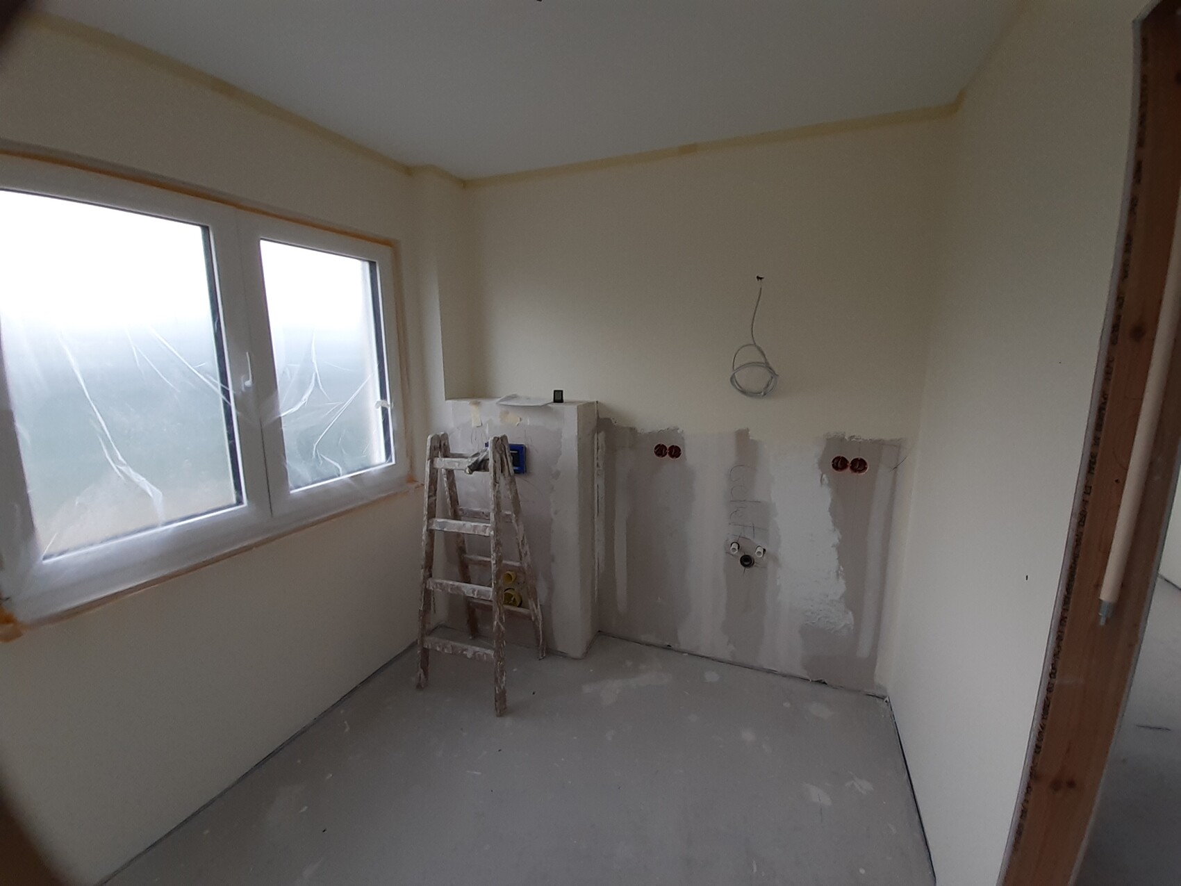 Renovierungsraum: Leiter steht vor einer Wand mit Installationsdosen, Kabel hängen, Fenster links.