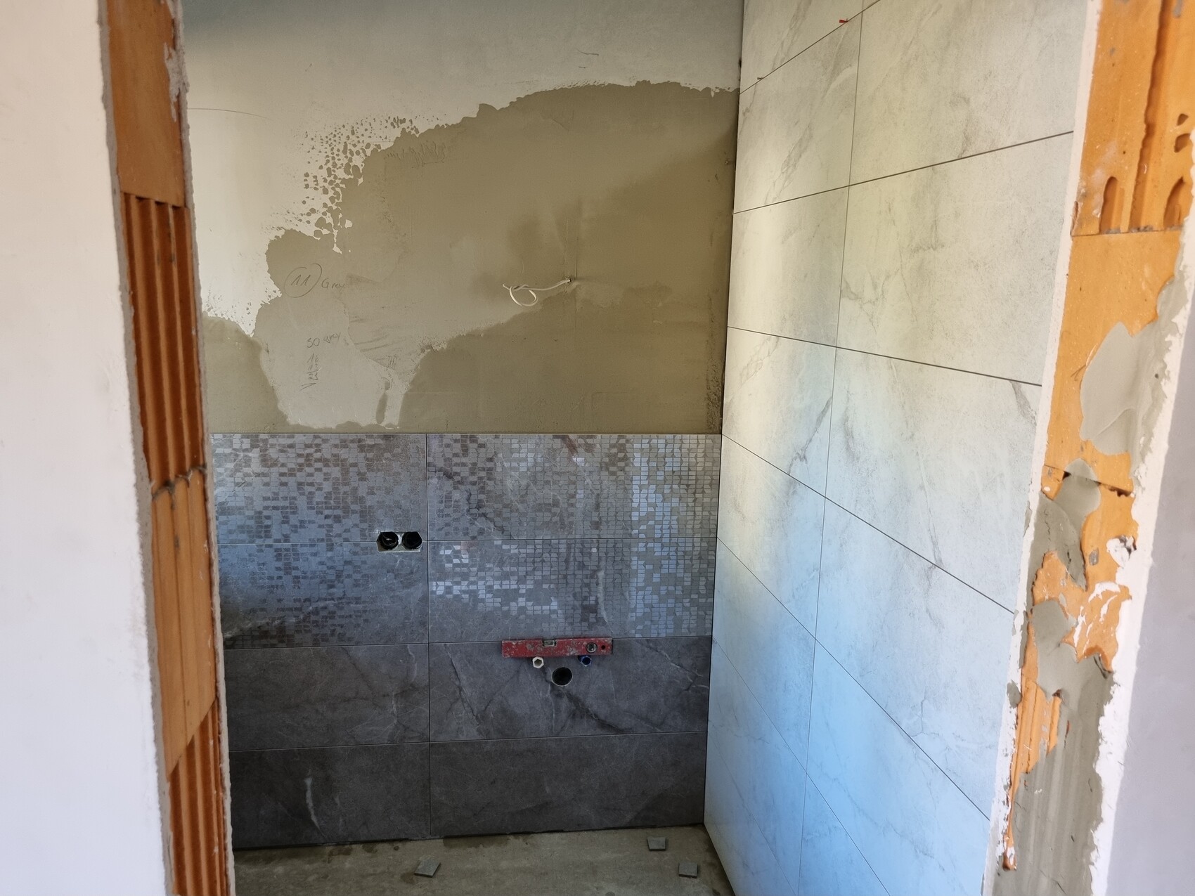 Badezimmer im Bau mit halb verlegten Fliesen, sichtbaren Rohren und unvollständigen Wänden
