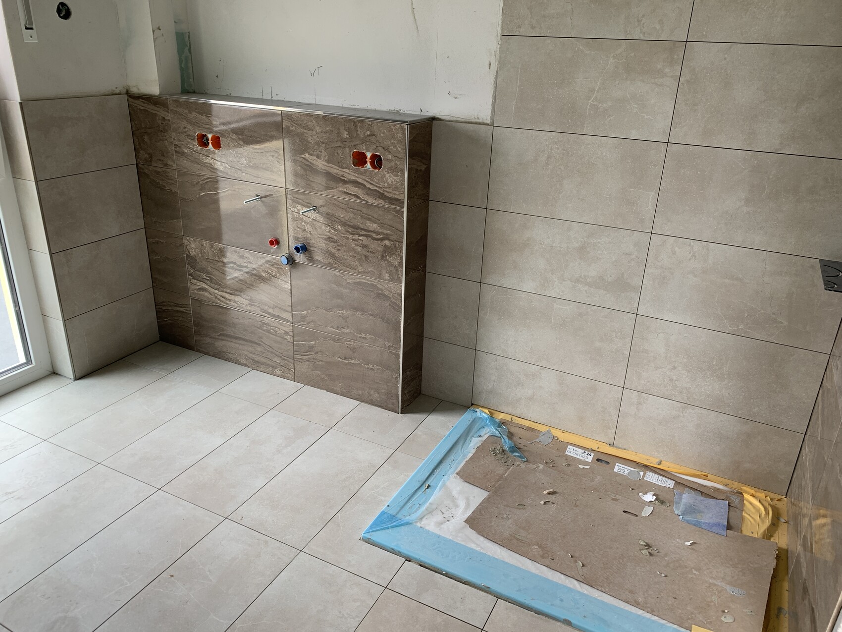 Badezimmer im Bau: Unterschrank mit Wasseranschlüssen, beige Boden- und Wandfliesen.