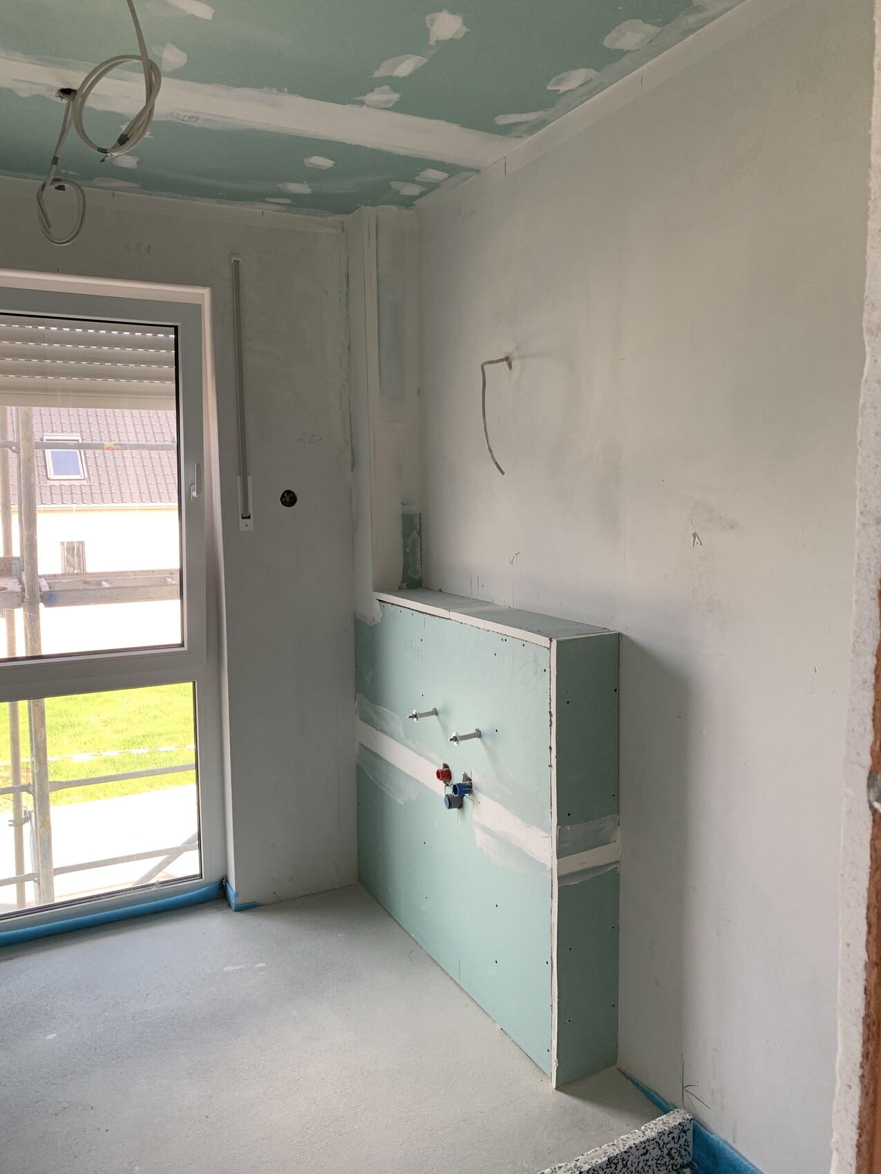 Renovierungsraum mit grünem Unterbaukasten, sichtbaren Wasseranschlüssen, Deckenputz und Fenster.