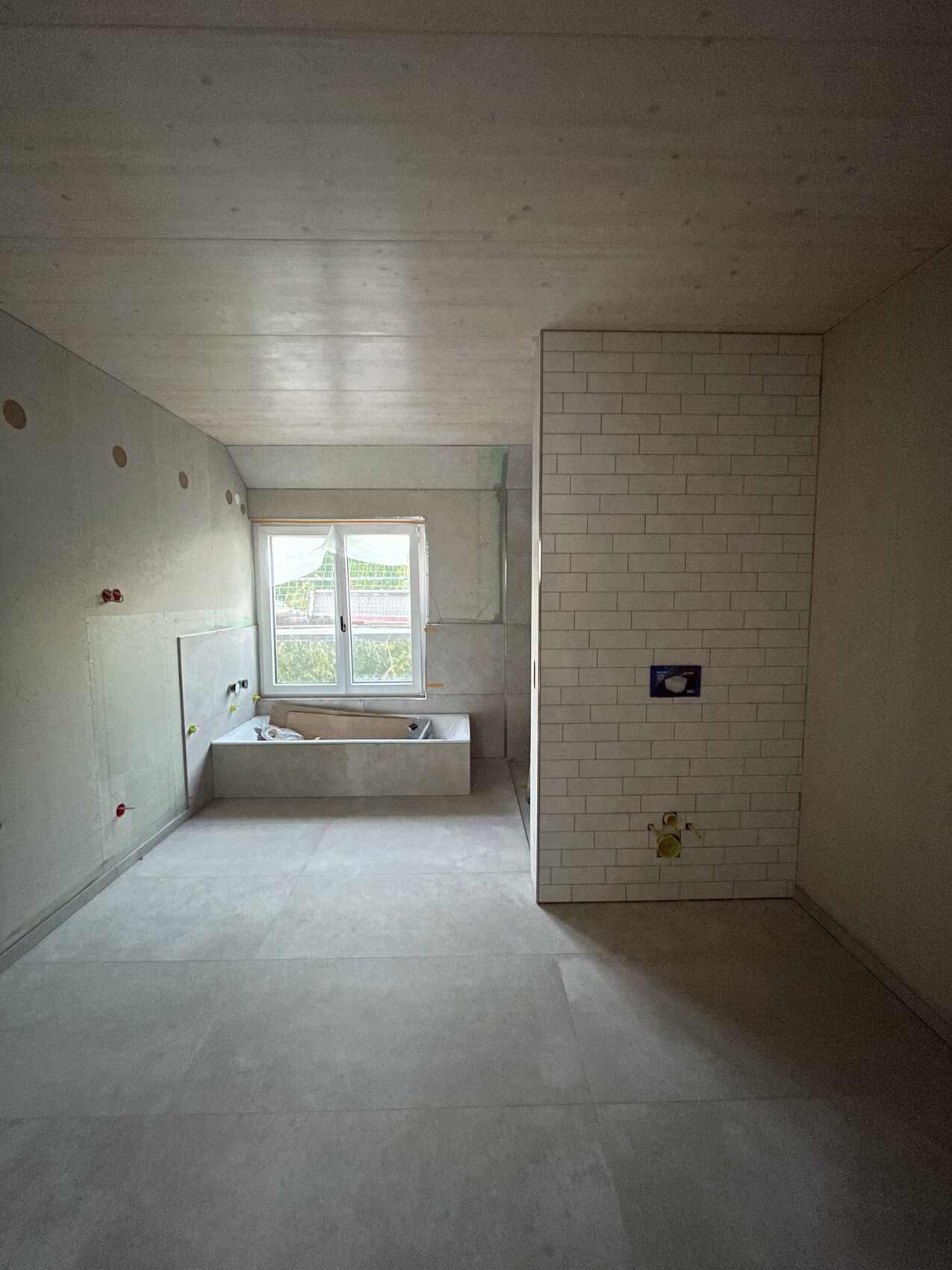 Rohbau-Bad: Badewanne am Fenster, linke Wand mit Löchern, rechte Fliesenwand