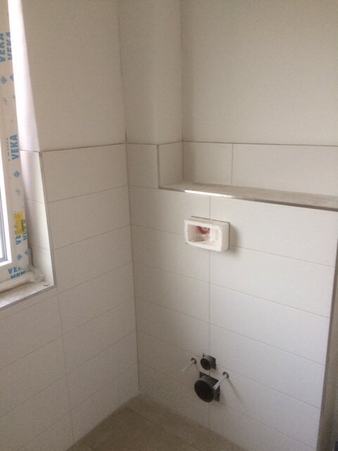 Bad mit weißen Fliesen, Sanitäranschlüssen und Fensterrahmen im Bau