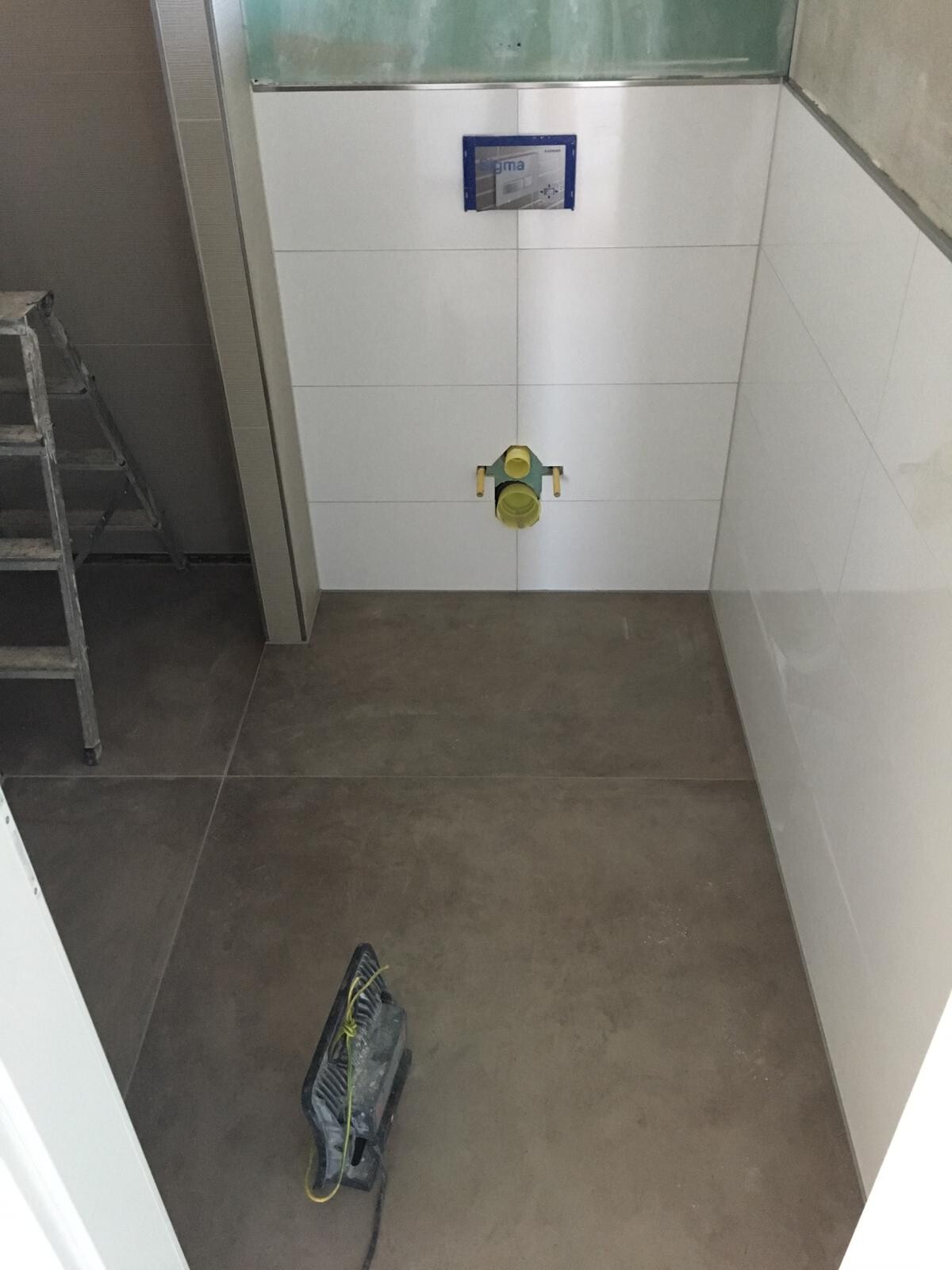 Baustellenbad: Fliesenwand mit gelbem WC-Rohranschluss und blauem Spülkasten.