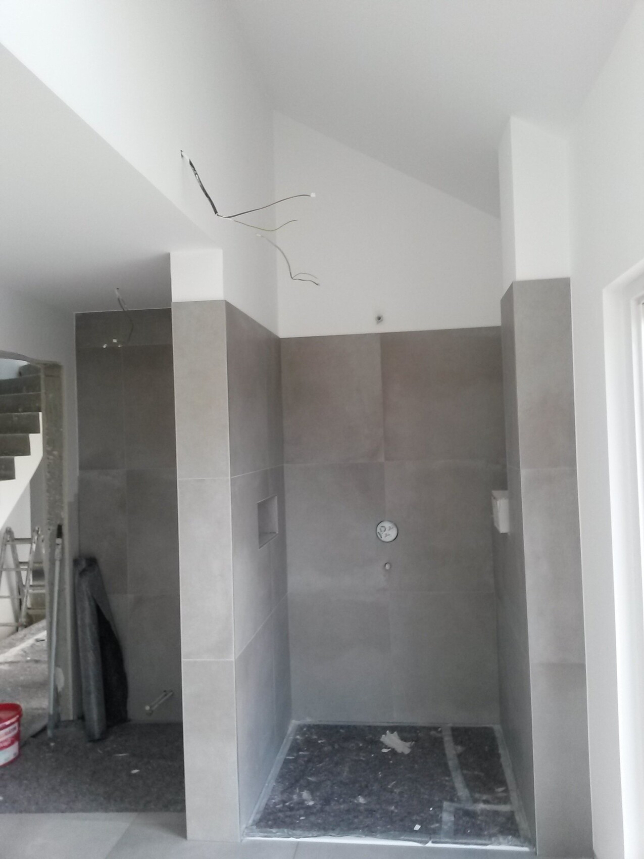 Bauphase: graue Fliesen in der Dusche, lose Kabel hängen von der Decke.