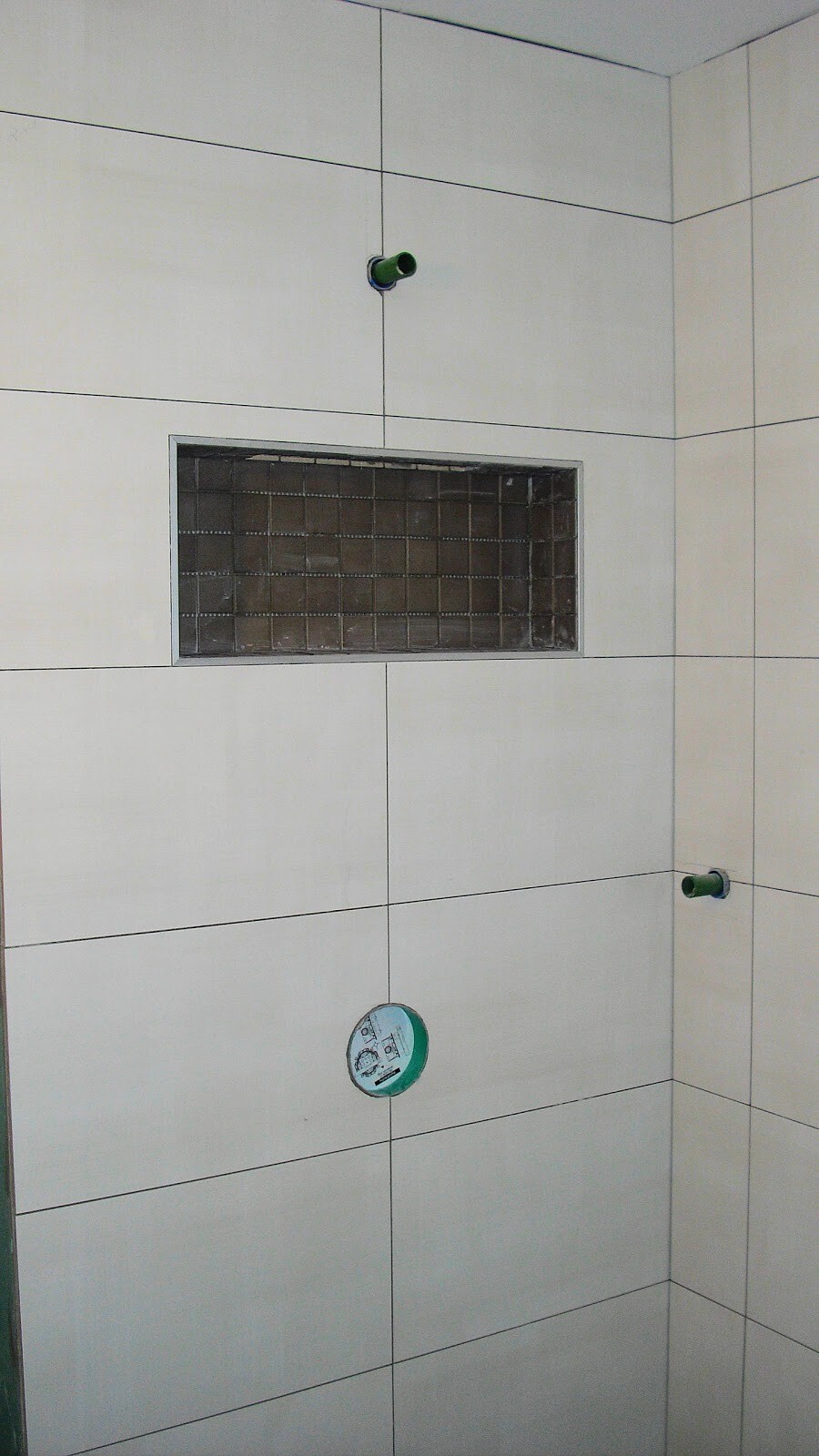 Badezimmerwand mit hellen Fliesen, offene Sanitärleitungen und Nische mit Metallgitter