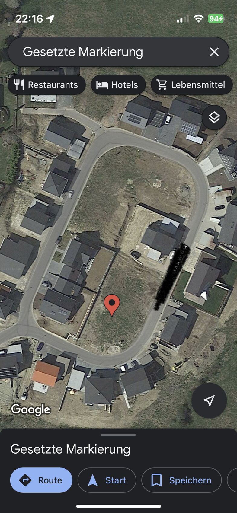 Satellitenaufnahme eines Wohngebiets mit Kreisstraße; roter Marker auf unbebautem Grundstück.
