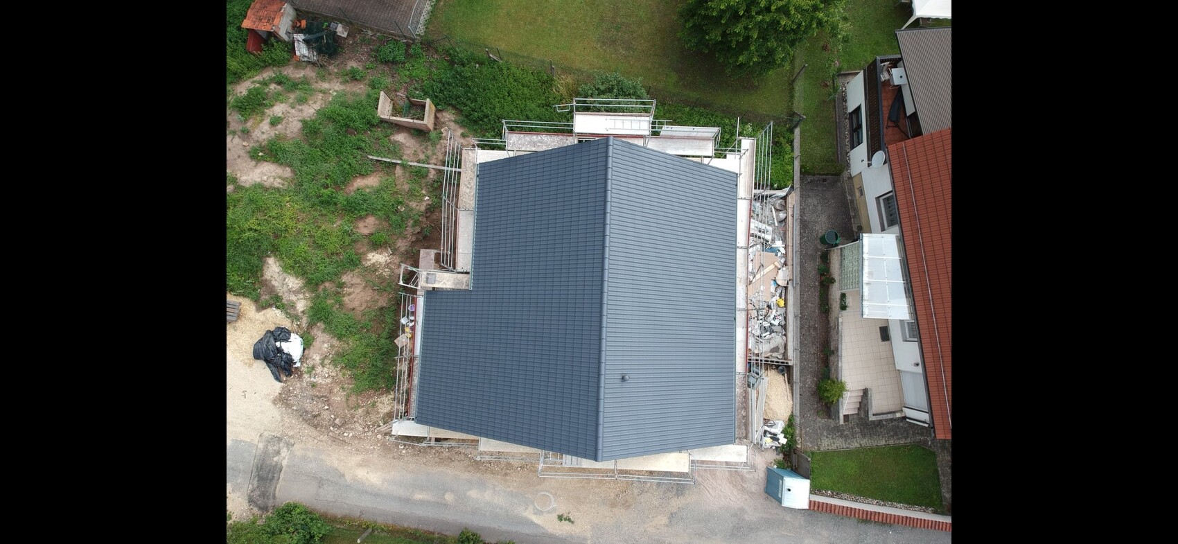 Vogelperspektive: Wohnhaus mit dunklem Metalldach, eingerüstet; Baustelle daneben.
