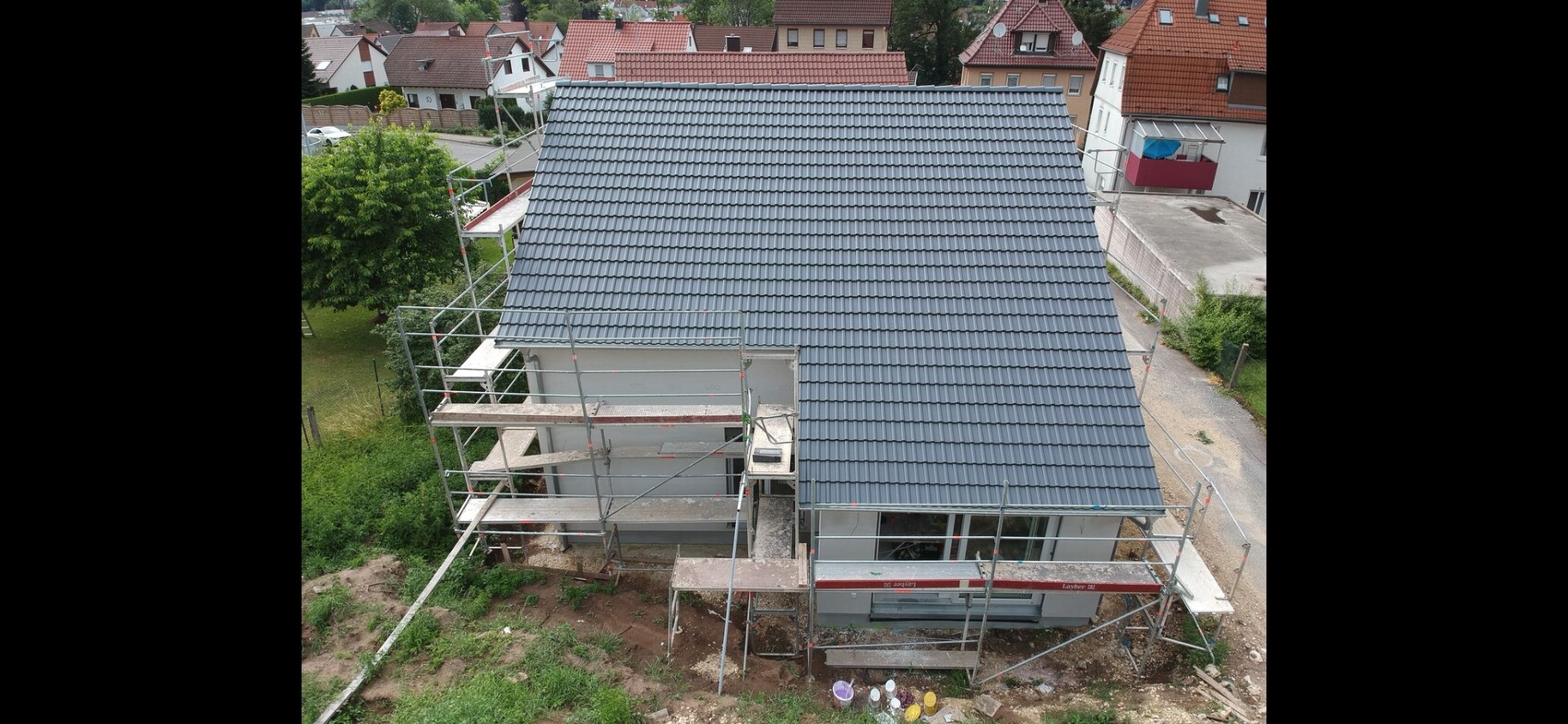 Drohnenaufnahme eines Hauses im Bau mit grauem Dach und umlaufendem Gerüst.